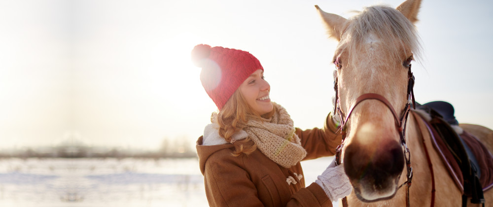 Frau mit Pferd auf einer Weide im Winter
